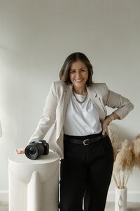 Smiling wedding and destination elopement photographer standing beside a camera in a bright studio, ready to capture authentic love stories.