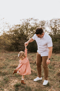 father twirling daughter in a field