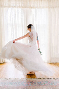 a bride twirls her dress in front of a window near omaha