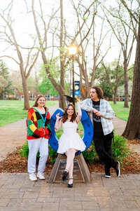 Senior girl sitting on the MTSU blue horseshoe with her two friends beside her