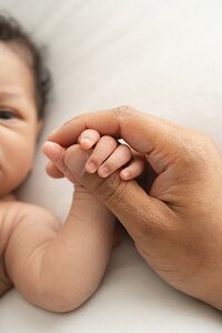 Louisville Portrait Photographer father holds newborn baby's hand during candid moment at Julie Brock Photography Studios