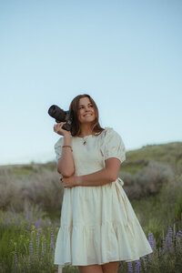Standing on a hill, Brittney looks off in the distance while holding her camera to her head.