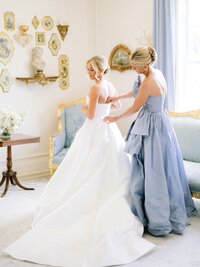 A wedding portrait of a bride and her mom zipping up her dress while getting ready at The Conservatory at Blackberry Ridge.