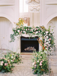 blush and white wedding florals with a lot of greenery around fire place for indoor ceremony backdrops  at dallas wedding venue the Olana with clear ghost chairs photographed by Tulsa Wedding Photographer Laura Eddy