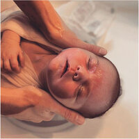 Deux mains tenant la tête d'un bébé, détendu dans son bain