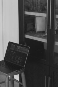A black and white photo of Michaela's laptop next to a modern bookshelf with decor in a photography studio in Bristol, TN