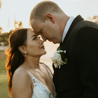 Bride and groom standing, foreheads touching, looking at each other. 