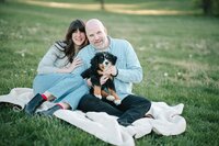 A couple sitting on a blanket smiling with a dog in their lap 
