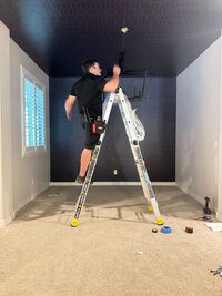 Installing chandelier against bold geometric wallpapered ceiling in a designer dining room.
