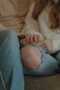 Close up of a couple resting their hands on her knee while sitting on a couch inside.