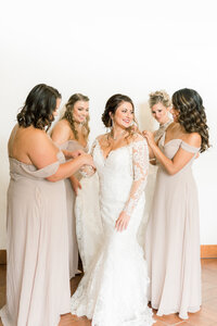 bride surrounded by her bridesmaids helping the bride put on her wedding dress at the estes park wedding venue black canyon inn
