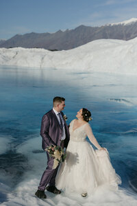 A couple standing a glacier next to a vibrant blue glacier pool. 