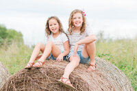 Two friends giggle while sitting on a bale of hay by Laramee Love Photography