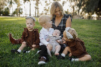 A picture of a mother with her four little children sitting on the grass posing for a candid photo