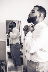 Groom adjusting his tie in the mirror during an artistic getting-ready moment before his wedding.