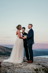 Couple exchanging vows during their Lake Tahoe elopement at Donner Summit, with soft sunset skies and panoramic mountain views in the distance.