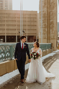 golden portrait of bride and groom walking along a bridge