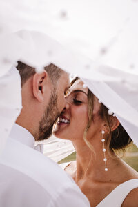A close-up of a couple kissing under a white, embellished veil.