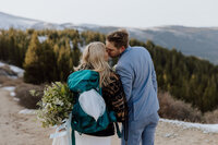 bride and groom kissing with mountains in background and a hiking backpack on the brides back