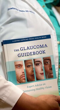 Dr. Constance Okeke in a white coat holding The Glaucoma Guidebook, symbolizing expert glaucoma care and trusted patient education.