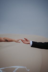bride and groom reach for each other and barely touch at sand dunes in Nevada