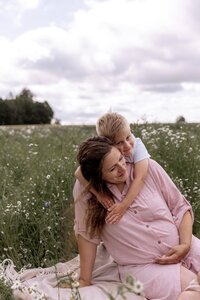 Mutter sitzt auf einer Decke auf einer Wiese und wird von ihrem Sohn umarmt
