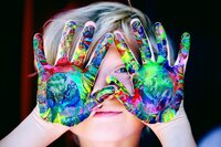 Child with finger paint on hands, hands up to face.