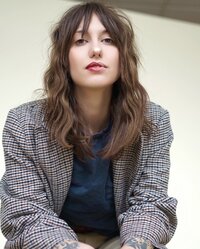 Woman sitting with a blazer and short brown hair with bangs