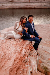 A man proposing to his partner on a sandy beach at Lake Powell, with the sun setting behind the couple and casting a golden glow over the water.