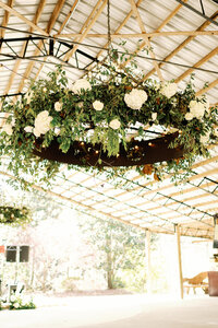 Vaulted ceilings with round chandelier hanging covered in greenery and white florals