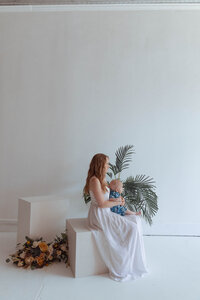 Mother cuddling newborn on modern lounge chair in photography studio