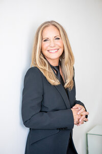 black and white image of a smiling woman in a dark blazer posing confidently with hands clasped in front