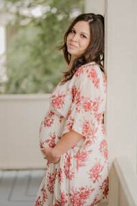 An expecting mama in a beautiful cream and floral gown holds her bump.