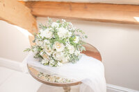 White rose bridal bouquet lying on a table with a veil
