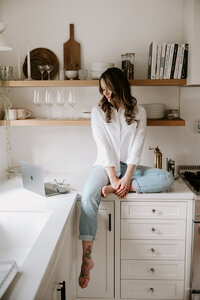 Freelance copywriter Erika Fitzgerald sitting on a kitchen counter, looking at an open laptop while working on web copy