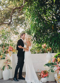 Film photo of bride and groom sharing their first kiss at their destination wedding ceremony in Costa Rica, surrounded by lush greenery and colorful florals.