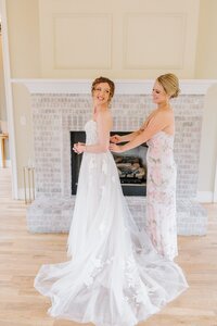 A bride finishes putting on her dress in front of the fireplace at the Bradford in NC.