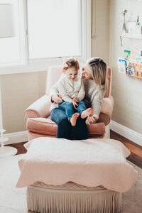 A cute mother and daughter sit together on a pink chair in their home during their lifestyle photography session with Christine Dammann