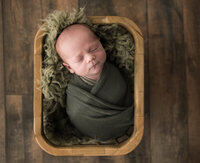 newborn baby boy wrapped in green swaddle for studio newborn portraits