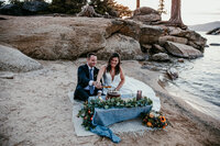 Couple celebrating with a styled picnic and mini cake on the rocks at sunset, captured by San Francisco elopement photographer Kristin Smith.