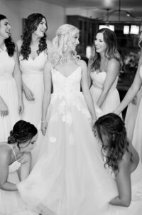 Wife-to-be shares a moment filled with laughter with her bridesmaids who adjust her wedding gown.