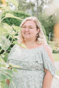 Faith, Moonstone’s Assistant Designer, smiling in a garden setting with sunflowers, wearing a light green floral dress.