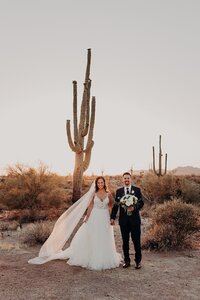 Couple stands side by side holding hands in front of a saguaro cactus