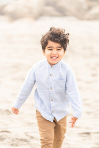 Little boy running on the beach straight towards the camera with a big smile