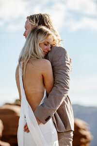 A bride and groom during their elopement in Moab at Dead Horse State Park. The couple is embracing, and the bride has her face resting on the shoulder of the groom