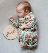 newborn baby girl with wooden sign that says it's a girl
