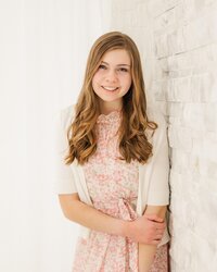 Girl, who is part of a North East, PA, family photography team, standing by a white wall.