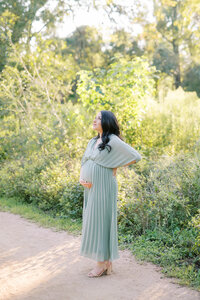 Husband and wife walk hand in hand through park during maternity session