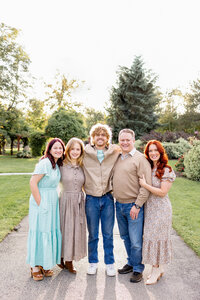 A family with three older children stand and smile for a gorgeous portrait.