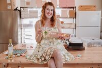 Baker sitting on a table holding a glass of wine and macarons during her branding photography session